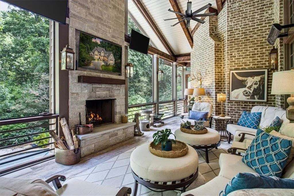 Screened outdoor living space featuring a stone fireplace, vaulted wood-beam ceiling, ceiling fan, and brick accent wall