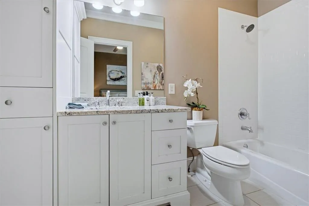 White vanity with a stone-finish countertop, under-mount sink, and chrome faucet