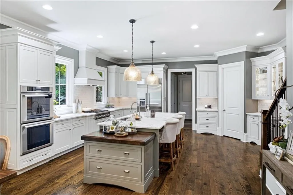 White cabinetry with crown molding, double ovens, a central island with wood-finish countertop, and wood-finish flooring