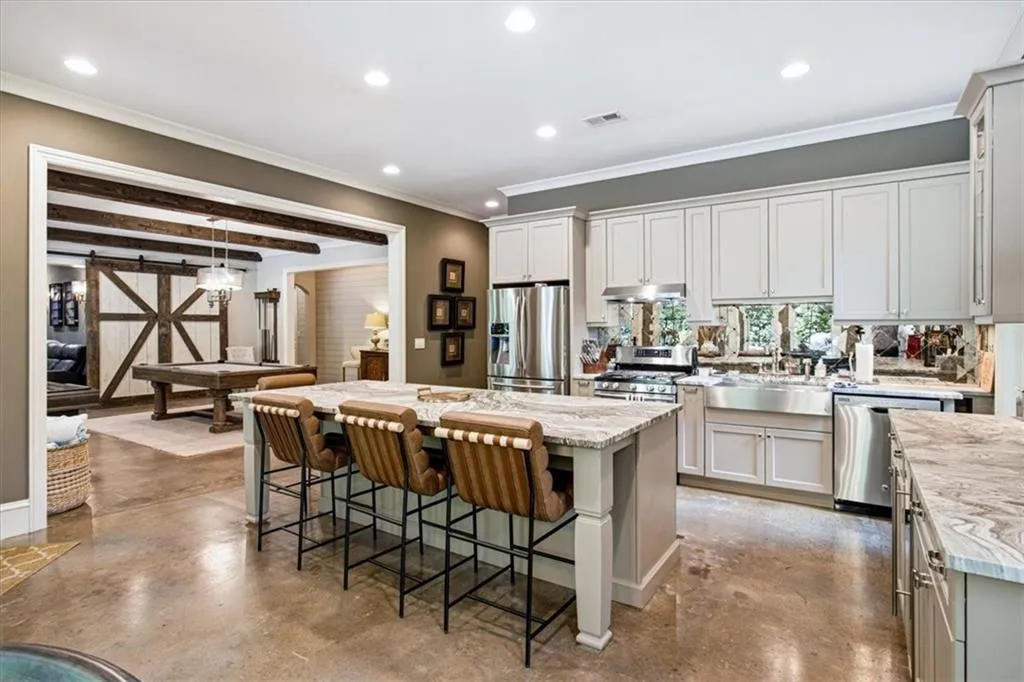 Kitchen featuring an island with a stone countertop, light-toned cabinetry, stainless steel appliances, and a farmhouse sink