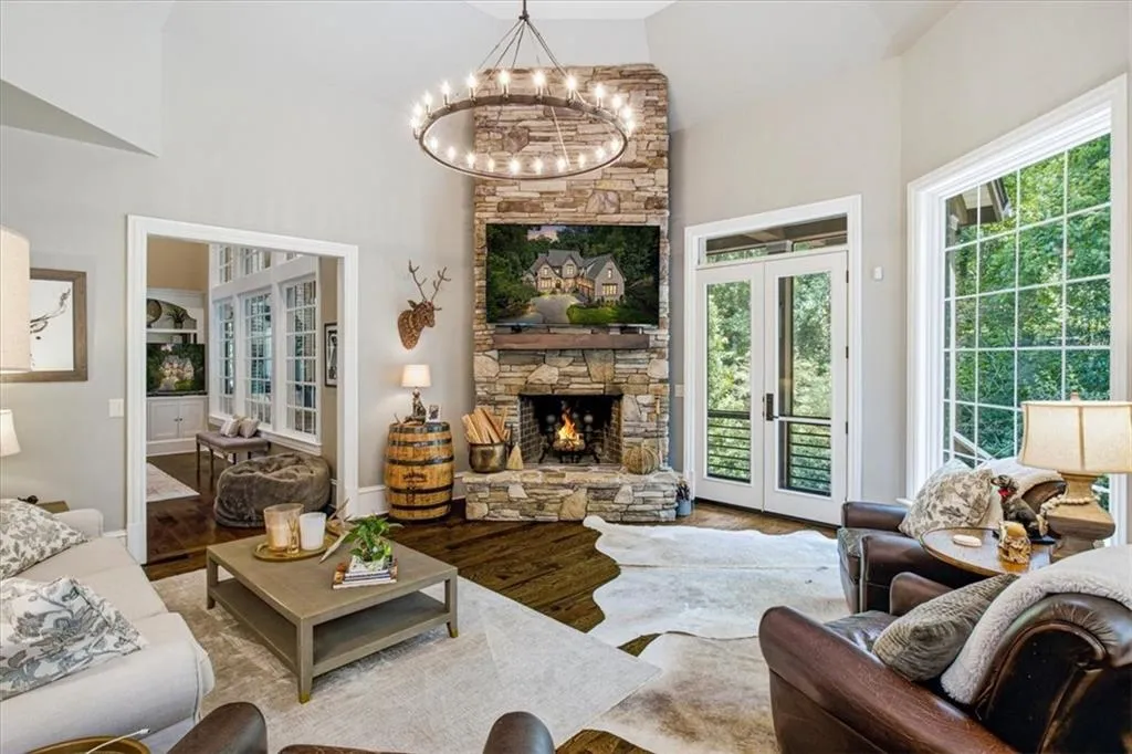 Vaulted ceilings, a stone-clad fireplace with a wood mantel, expansive grid-pattern windows, and hardwood flooring
