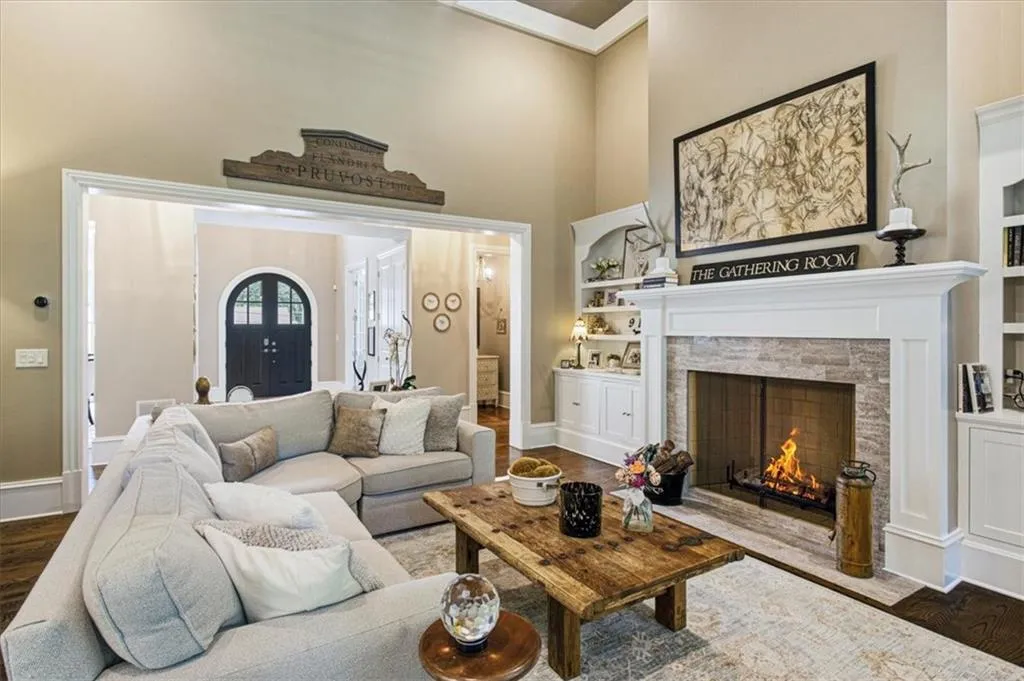 Spacious living area featuring a stone-surround fireplace with a white mantel, built-in shelving, and dark wood-finish flooring