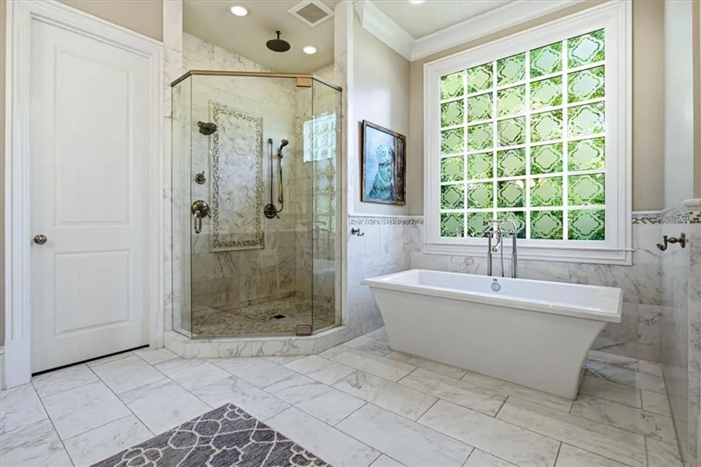 Freestanding soaking tub with floor-mounted faucet, an enclosed shower with multiple showerheads and decorative tile accent, and tiled flooring