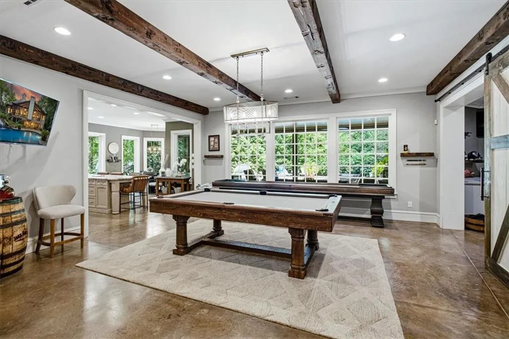 Exposed wood beams, expansive windows, concrete-finish flooring, recessed lighting, and a modern chandelier