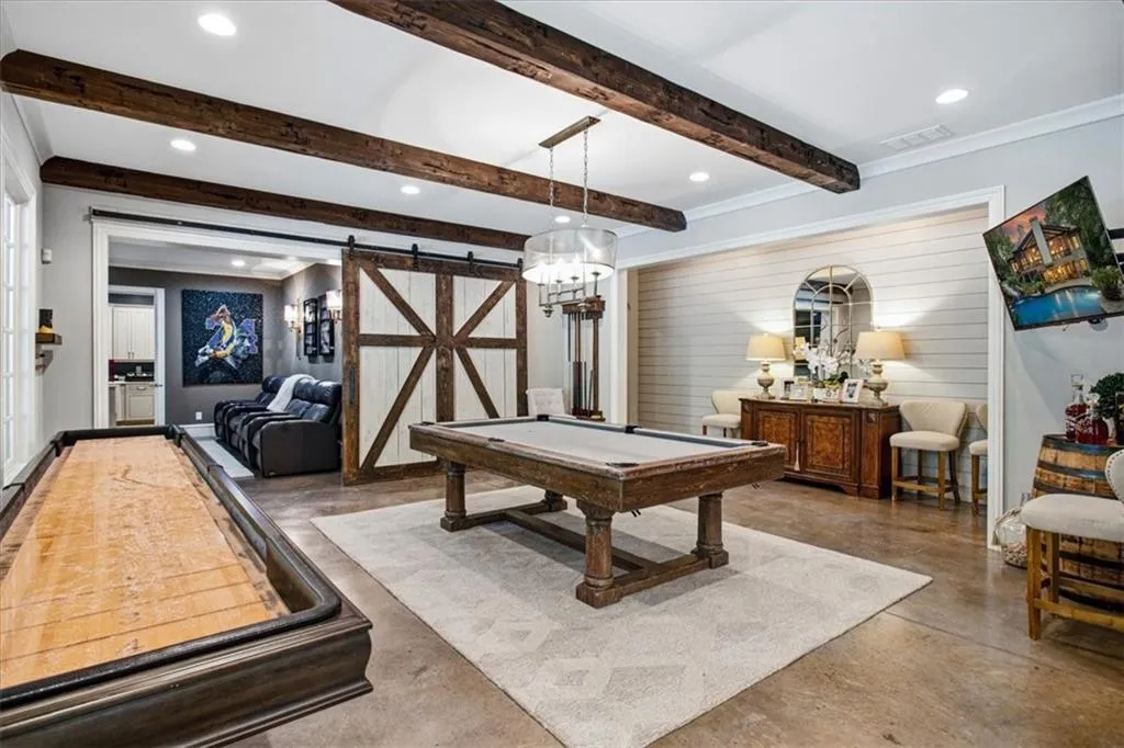 Exposed wood beams, concrete flooring, shiplap wall accent, barn door entry, and recessed lighting
