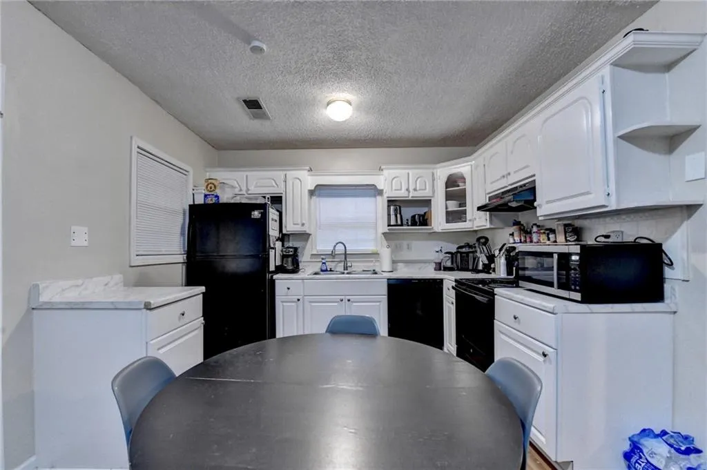 Kitchen featuring light countertops, open shelves, white cabinets, black appliances, and a textured ceiling