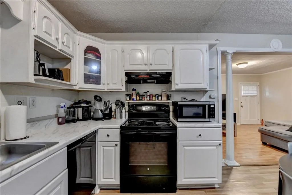 Kitchen with black appliances, light countertops, white cabinets, light wood-style floors, and glass insert cabinets