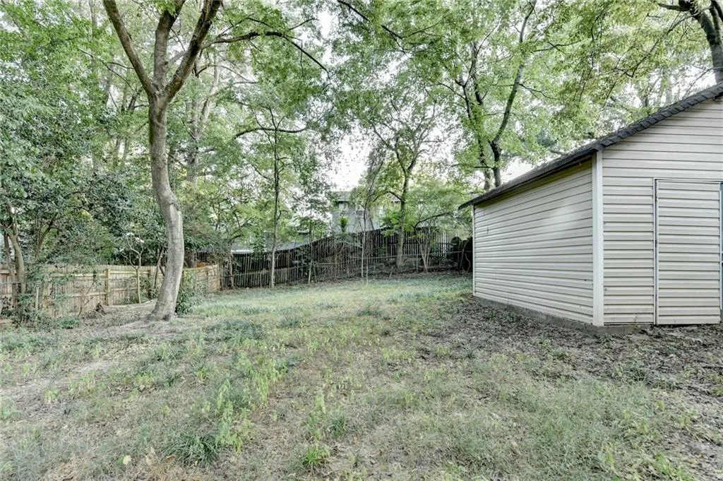 Fenced backyard with view of wooded area and an outbuilding