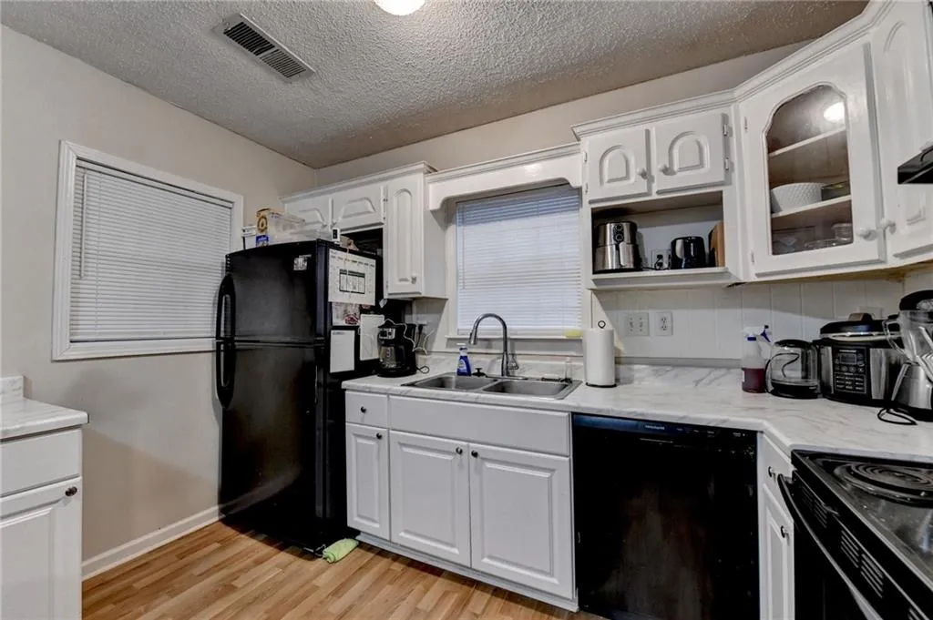 Kitchen with black appliances, light countertops, white cabinetry, light wood-type flooring, and open shelves