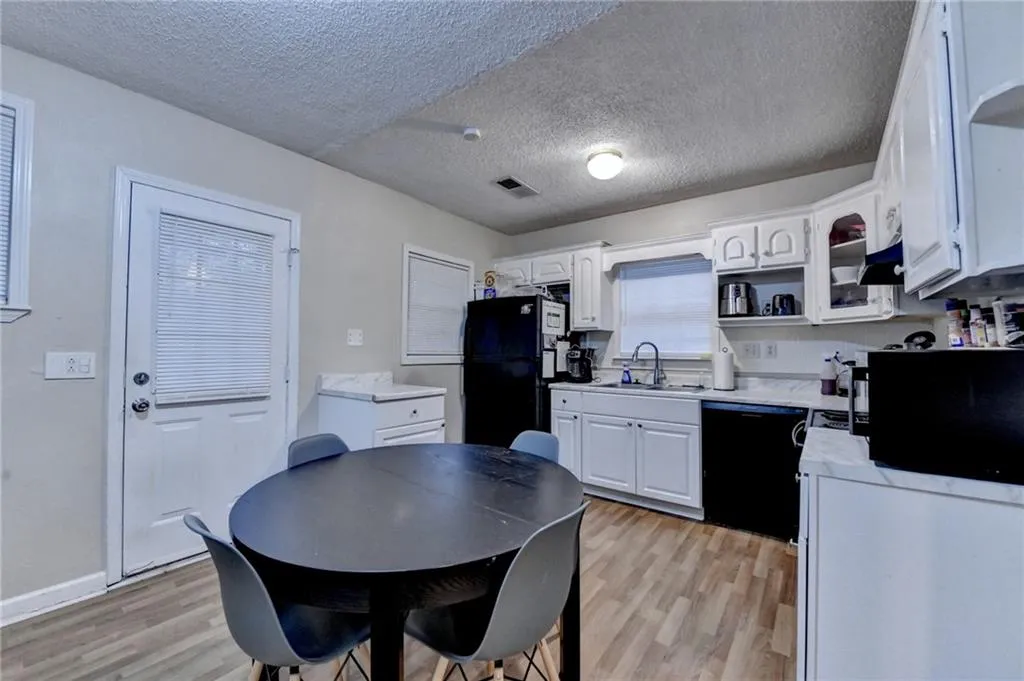 Kitchen featuring light countertops, white cabinetry, a textured ceiling, light wood-type flooring, and black appliances