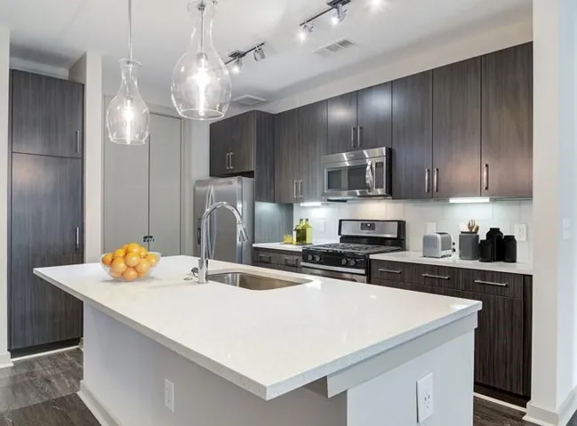 Kitchen featuring appliances with stainless steel finishes, rail lighting, a kitchen island with sink, dark hardwood / wood-style floors, and hanging light fixtures