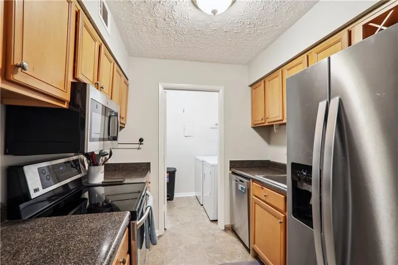 Kitchen with washer and dryer, a textured ceiling, light tile flooring, and appliances with stainless steel finishes