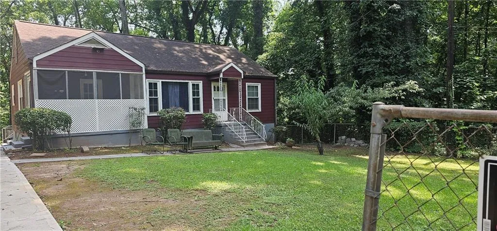 Red exterior siding, screened porch with lattice detailing, front entry porch with railing, mature trees, and a front lawn