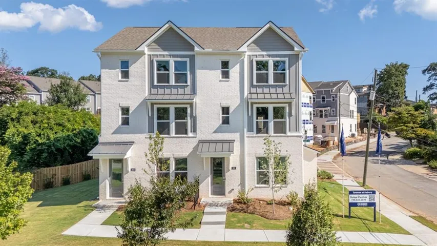 Modern townhouse exterior featuring white stucco, gray siding accents, multiple windows, and a paved walkway