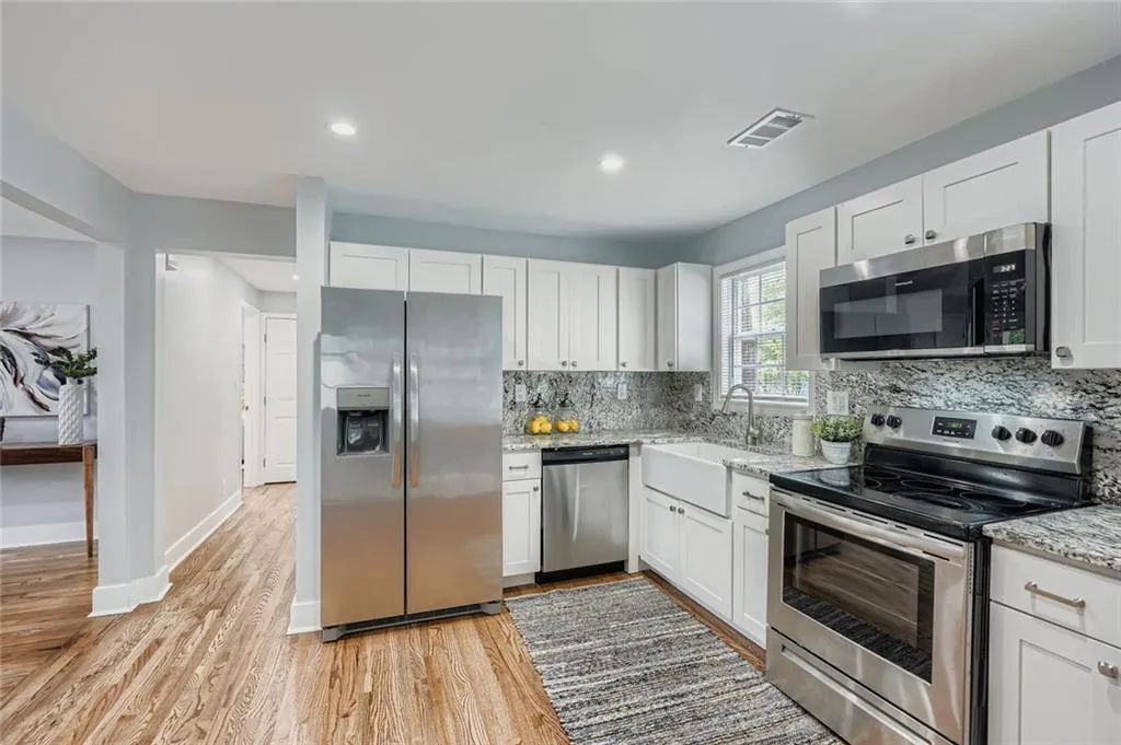 Another view of the updated kitchen with white cabinets, stainless steel appliances and granite counters.  Hall leads to two bedrooms on main.