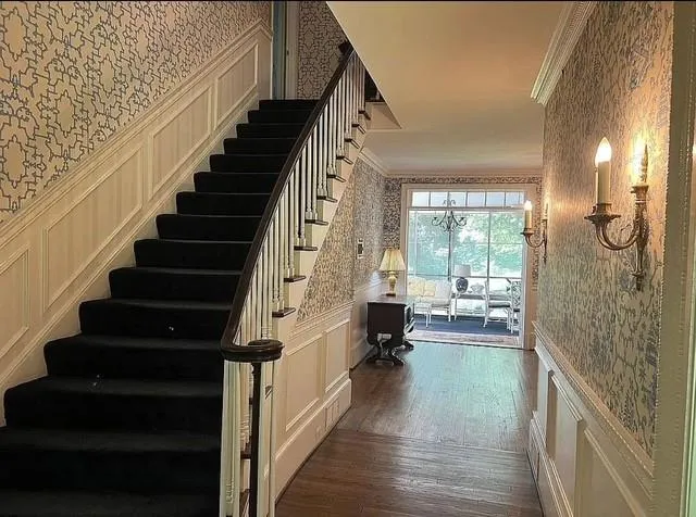 Stairway with wallpapered walls, wainscoting, a decorative wall, hardwood / wood-style flooring, and crown molding