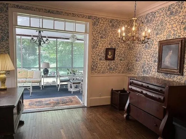 Dining room with wallpapered walls, a chandelier, a wainscoted wall, dark wood finished floors, and crown molding