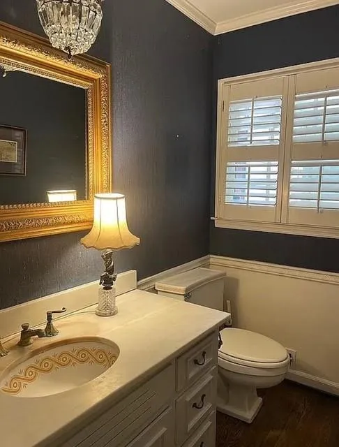 Half bath featuring vanity, ornamental molding, and wood finished floors