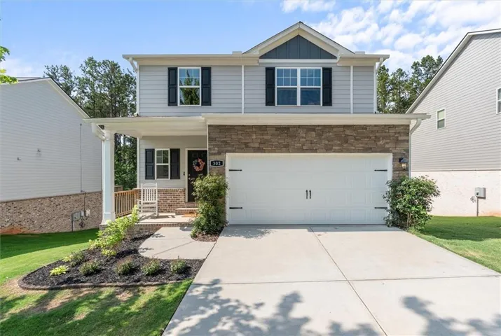 Two-story residence featuring a covered front porch, a stone-accented facade, and an attached garage with decorative hardware