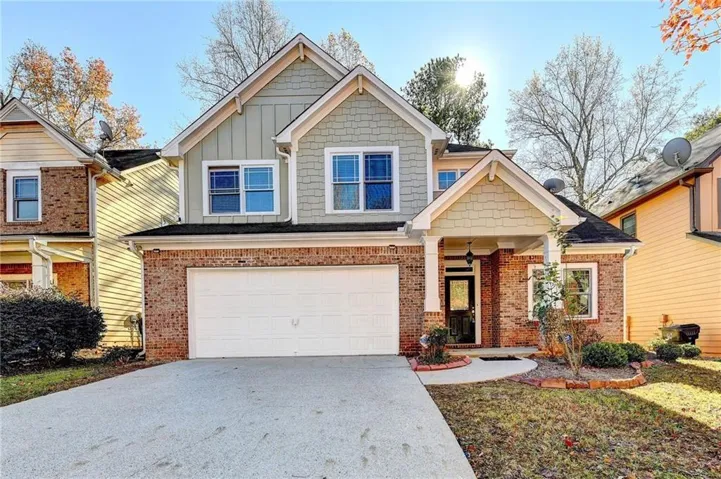 Brick and siding exterior featuring a covered entry porch, an attached garage, and a concrete driveway