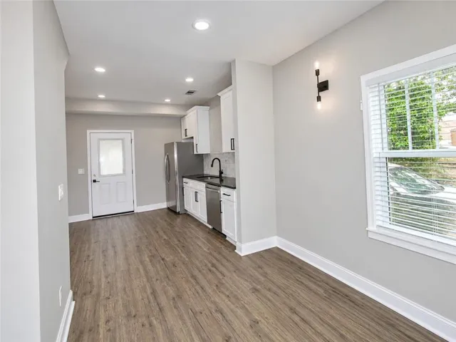 Recessed ceiling lighting, wood-finish flooring, white cabinetry, stainless steel appliances, and a black wall-mounted light fixture
