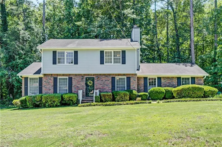 Traditional-style residence featuring a brick facade with light-colored siding, black louvered shutters, and a prominent front entrance with white railings