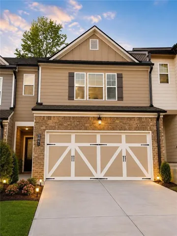 Two-story facade with brick and siding, a decorative garage door, and accent lighting