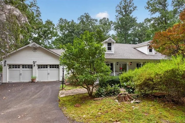 Charming colonial-style residence featuring a two-car garage with paneled doors, front-facing covered porch with columns, and dormer windows
