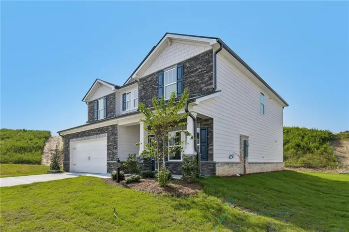 Two-story property featuring a stone and siding facade, a two-car garage, and dark window shutters