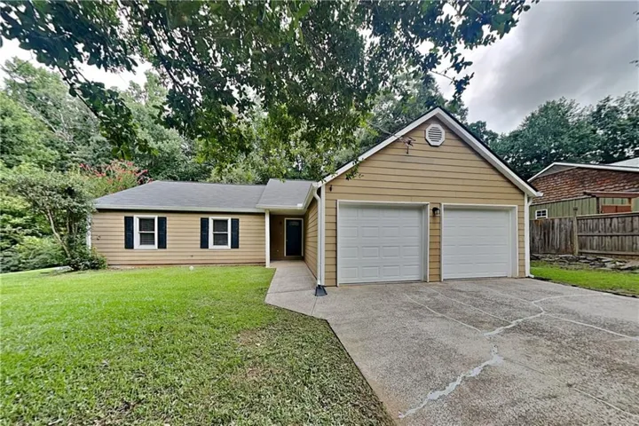 Single-story exterior with light brown siding, a two-car garage, a concrete driveway, and a front yard with mature landscaping