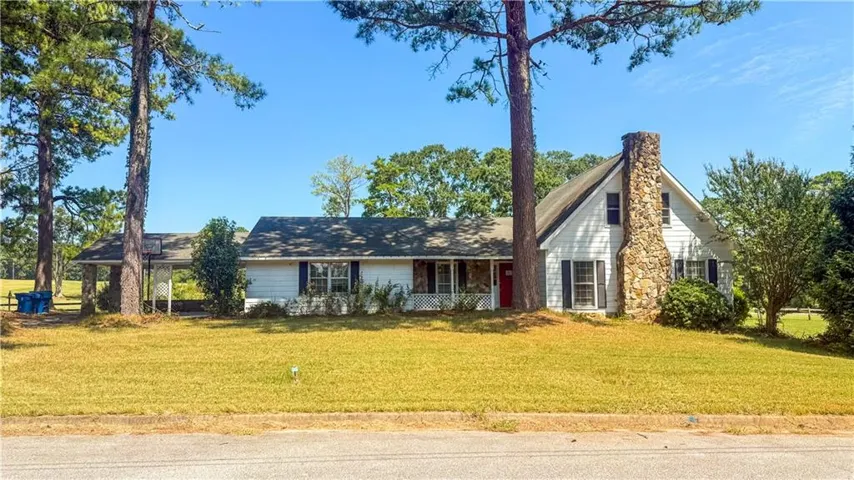 White siding exterior with a prominent stone chimney, a covered front porch, and a covered carport