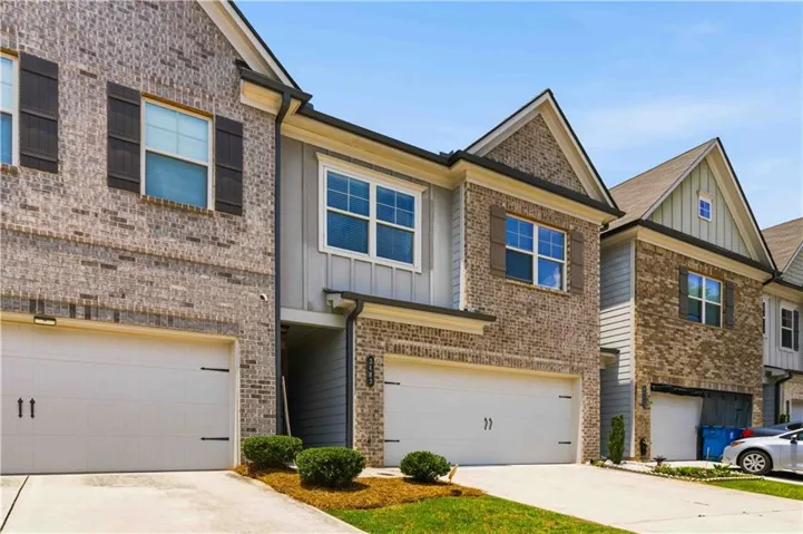 Brick and siding facade townhome featuring a two-car garage, dark decorative shutters, gabled rooflines, and concrete driveway