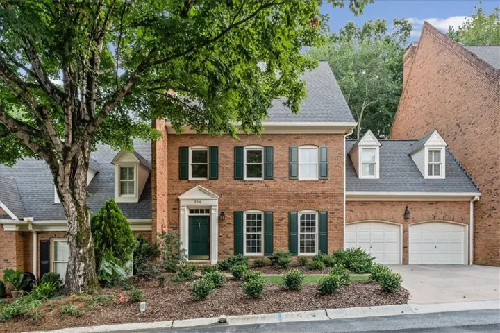 Brick exterior featuring a two-car garage, dormer windows, and a prominent front entrance with a deep green door
