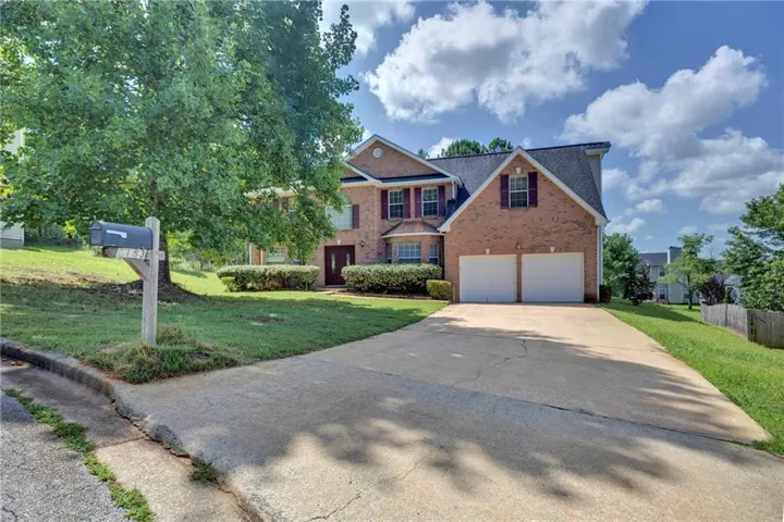 Traditional brick-front residence featuring a two-car garage, established front landscaping, a paved driveway, and a gabled roofline