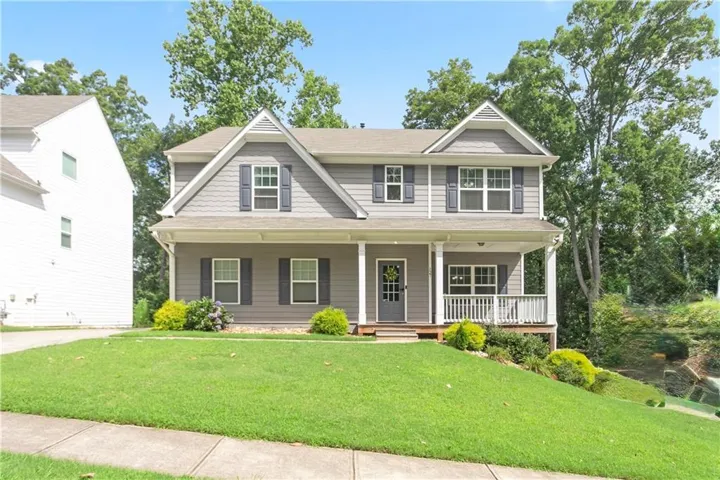 Gray two-story residence featuring a covered front porch with white railings, a front door with decorative glass, and dark window shutters