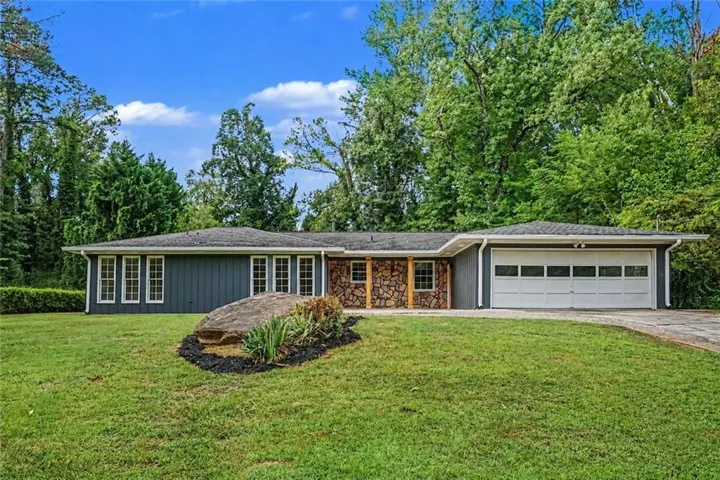 Stone veneer facade with wood accents, multiple front-facing windows, attached garage with a sectional door, and a landscaped front yard with a large natural rock feature