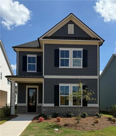 Two-story residence featuring dark gray siding, white window trim, black shutters, brick foundation, and a covered porch entry