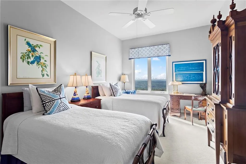 Bright room with twin beds, featuring a multi-pane window with a patterned valance, and a ceiling fan
