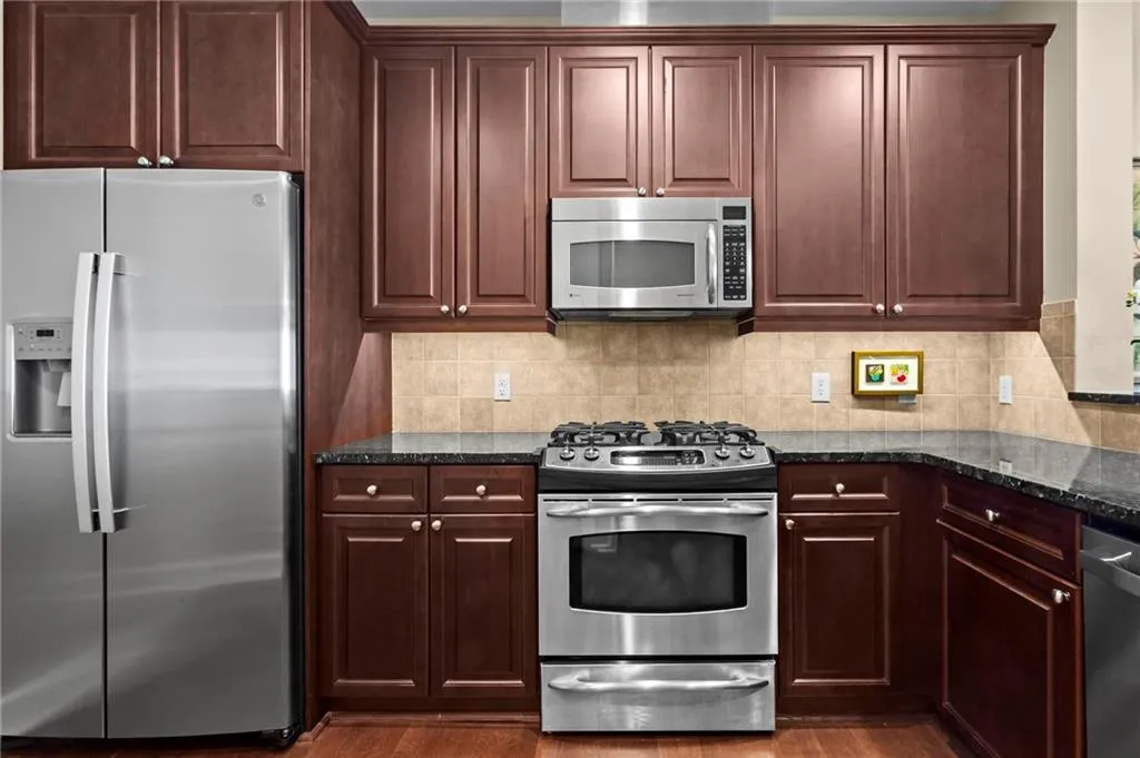 Stainless steel appliances, wood cabinetry, a tile backsplash, and a built-in microwave