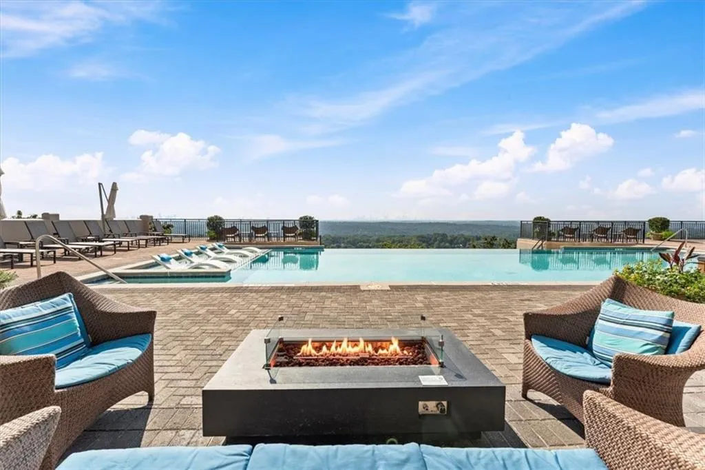 Pool deck featuring an infinity-edge pool, facing the Atlanta skyline with multiple lounge areas, a modern fire pit, and paver flooring