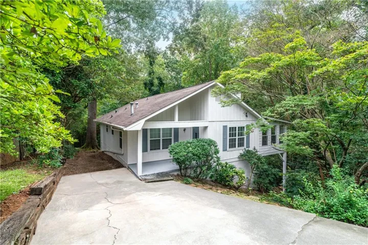 Ranch-style house featuring a shingled roof, view of wooded area, and driveway