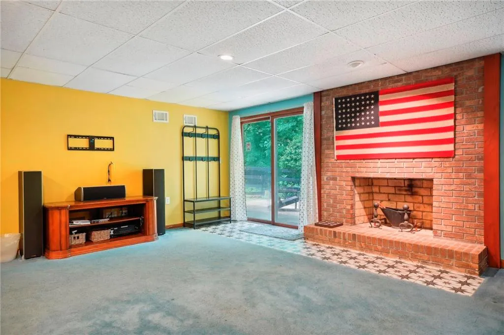 Unfurnished living room featuring carpet flooring, a brick fireplace, and a drop ceiling