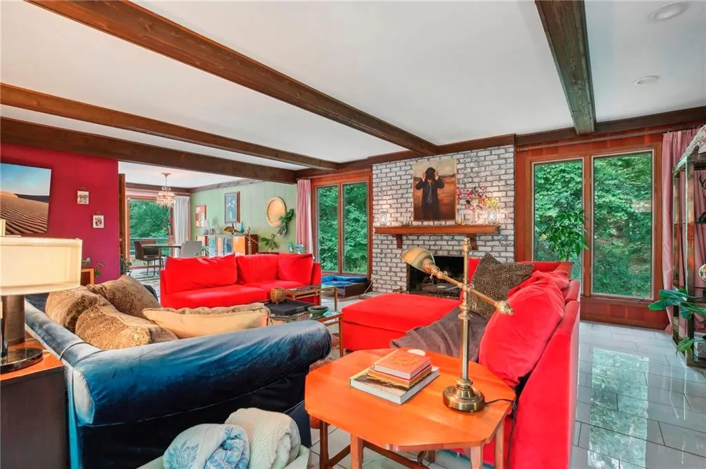 Tiled living room featuring beam ceiling, a healthy amount of sunlight, a fireplace, and brick wall