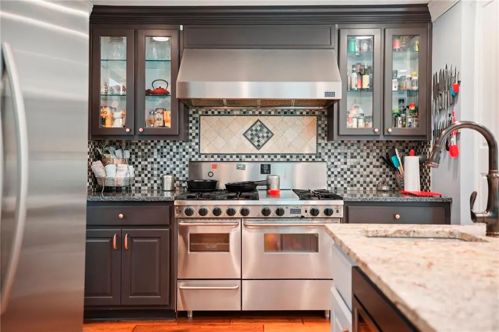 Kitchen with range hood, stainless steel appliances, hardwood / wood-style flooring, and tasteful backsplash