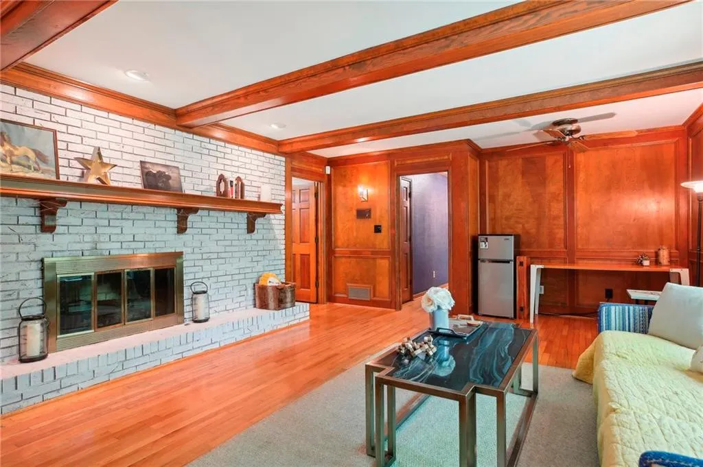 Living room featuring a brick fireplace, ceiling fan, beamed ceiling, and hardwood / wood-style flooring