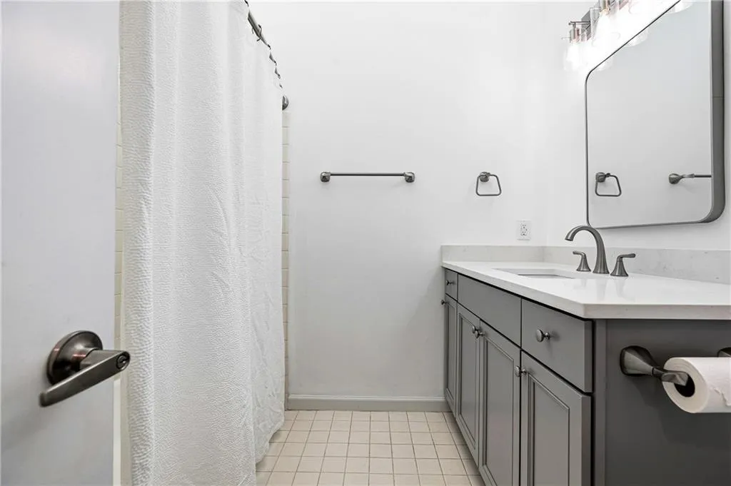 Bathroom featuring a gray vanity with a white countertop, coordinating gray mirror frame, brushed nickel faucet, and square tile flooring
