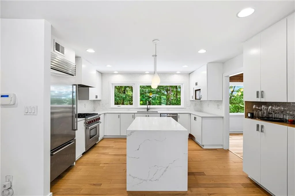 Bright kitchen featuring white cabinetry, a large center island with a waterfall countertop, stainless steel appliances, and wood-finish flooring