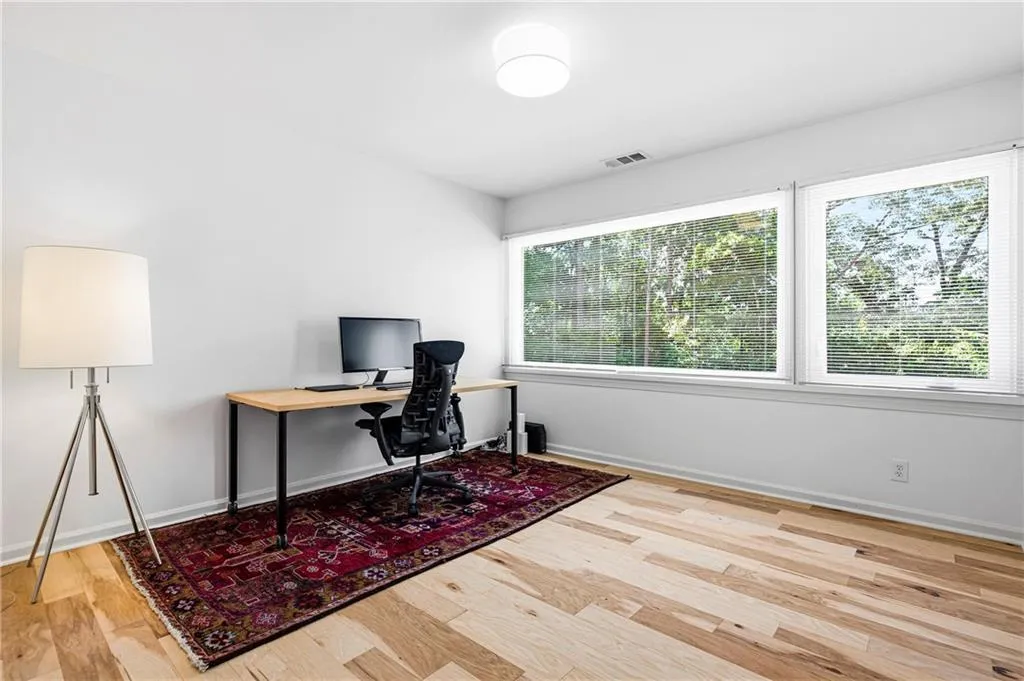 Bright room featuring two large windows with blinds, wood-finish flooring, and a flush-mount ceiling light fixture