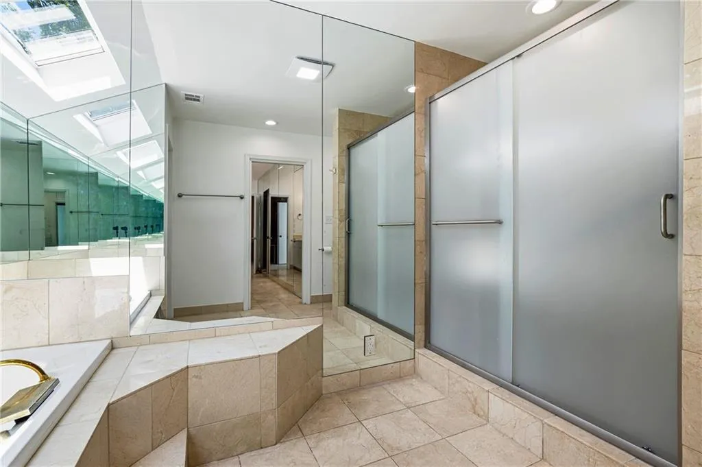 Bathroom featuring a large built-in tub with a white surface, skylights, extensive mirror paneling, and a frosted glass shower enclosure