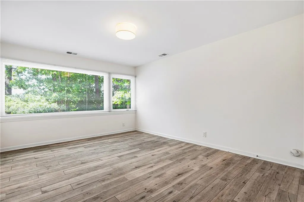 Spacious room featuring expansive windows, wood-finish flooring, white walls, and a contemporary ceiling light fixture
